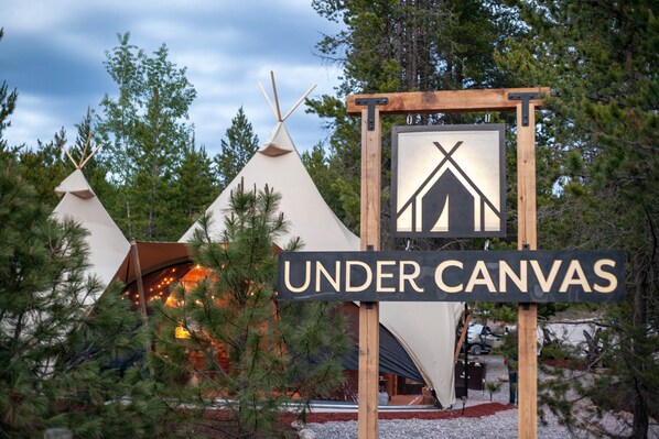 A sign for 'Under Canvas' with teepees in the background.