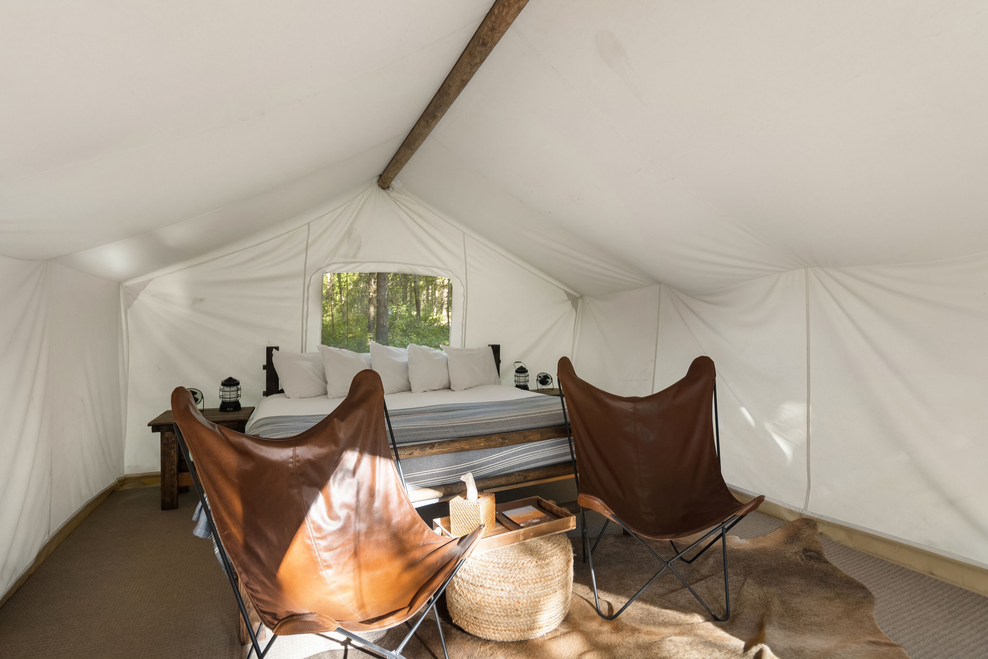 Una tenda arredata con un letto, due poltrone in pelle, un tavolino e una finestra vista alberi.