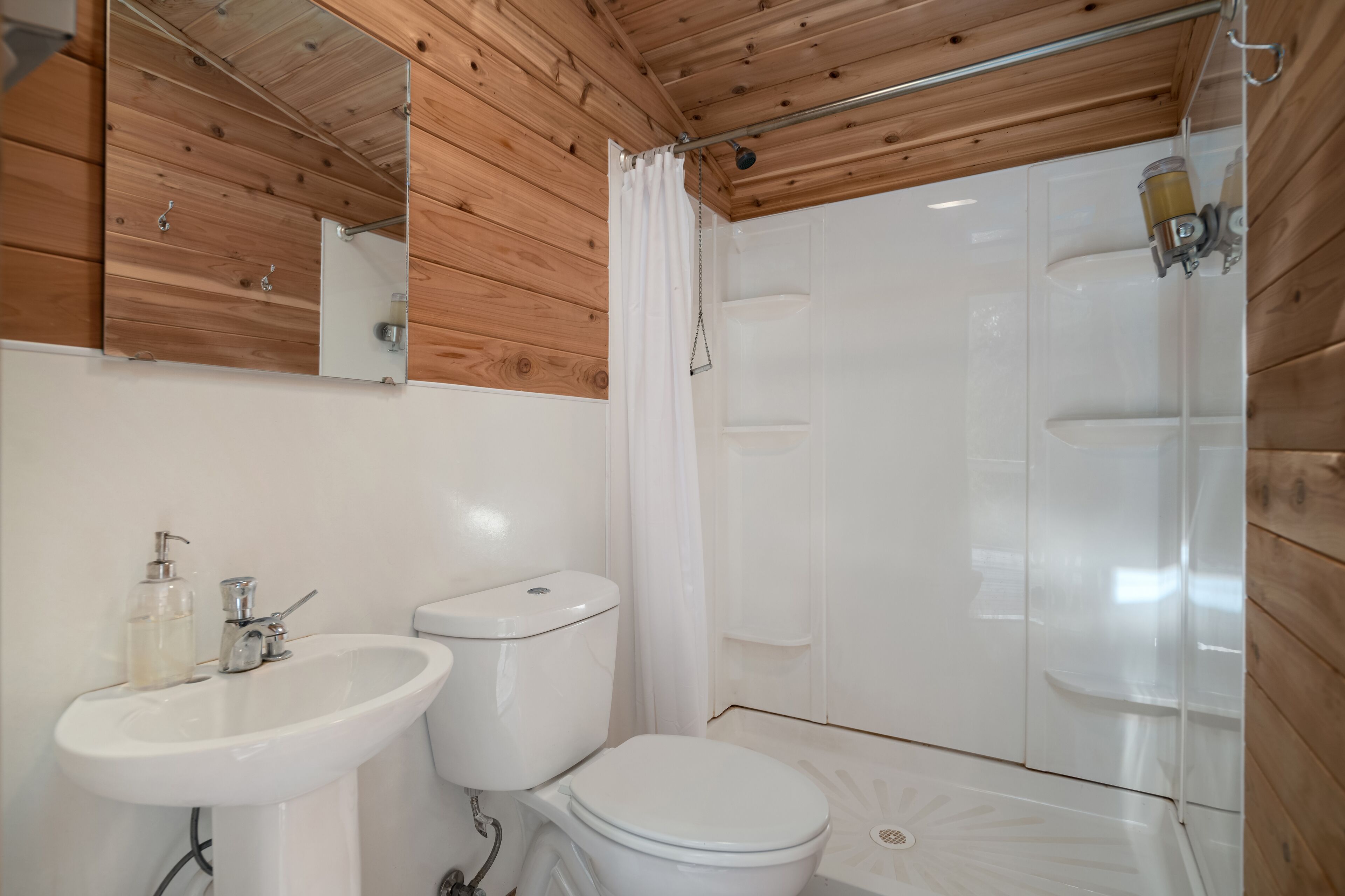 A bathroom with a wooden ceiling, a white sink, a toilet, and a shower enclosure.