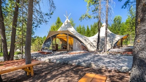 A forested campsite with teepee-style tents and picnic tables. - Under Canvas Glacier (Coram)