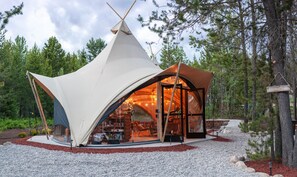 A modern, semi-open structure with a glass facade, surrounded by a gravel path and forest. - Under Canvas Glacier (Coram)