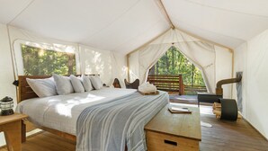 A tented room with a bed, a wooden table, and a view of the forest. - Under Canvas Glacier (Coram)