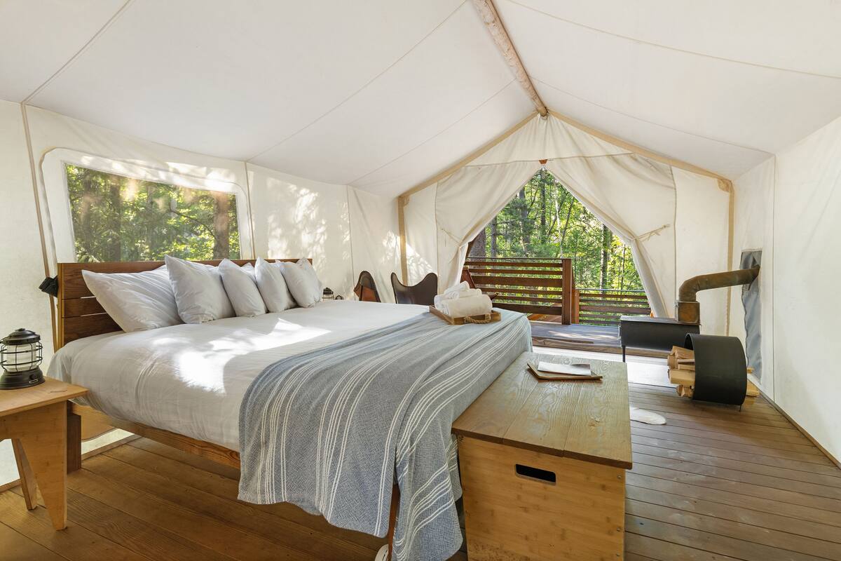 Una habitación con carpa, una cama, una mesa de madera y vistas al bosque.