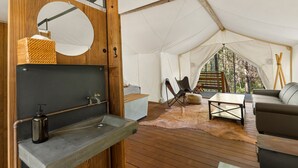A tent with a wooden floor, a sink, a mirror, a chair, and a sofa. - Under Canvas Glacier (Coram)