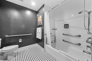 A modern bathroom with a black and white checkered floor, a glass-enclosed shower, and a toilet with a handrail. - Le Bon Hotel Hollywood (Los Angeles)