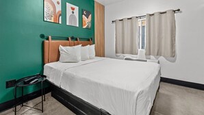 A neatly arranged bedroom with a bed, a bedside table, and a window with curtains. - Le Bon Hotel Hollywood (Los Angeles)
