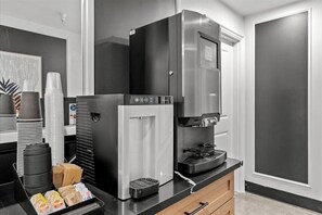 A kitchenette with a refrigerator, coffee maker, and stacked cups. - Le Bon Hotel Hollywood (Los Angeles)