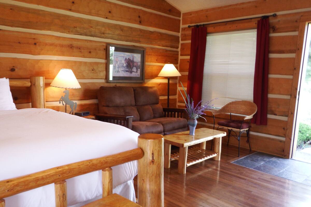 A log cabin room with a bed, two sofas, a small table, and a window with curtains.