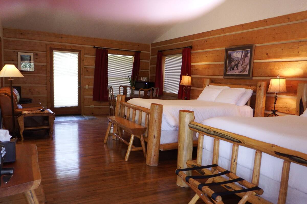 A wooden cabin-style room with two beds, a wooden bench, a desk, and a chair.