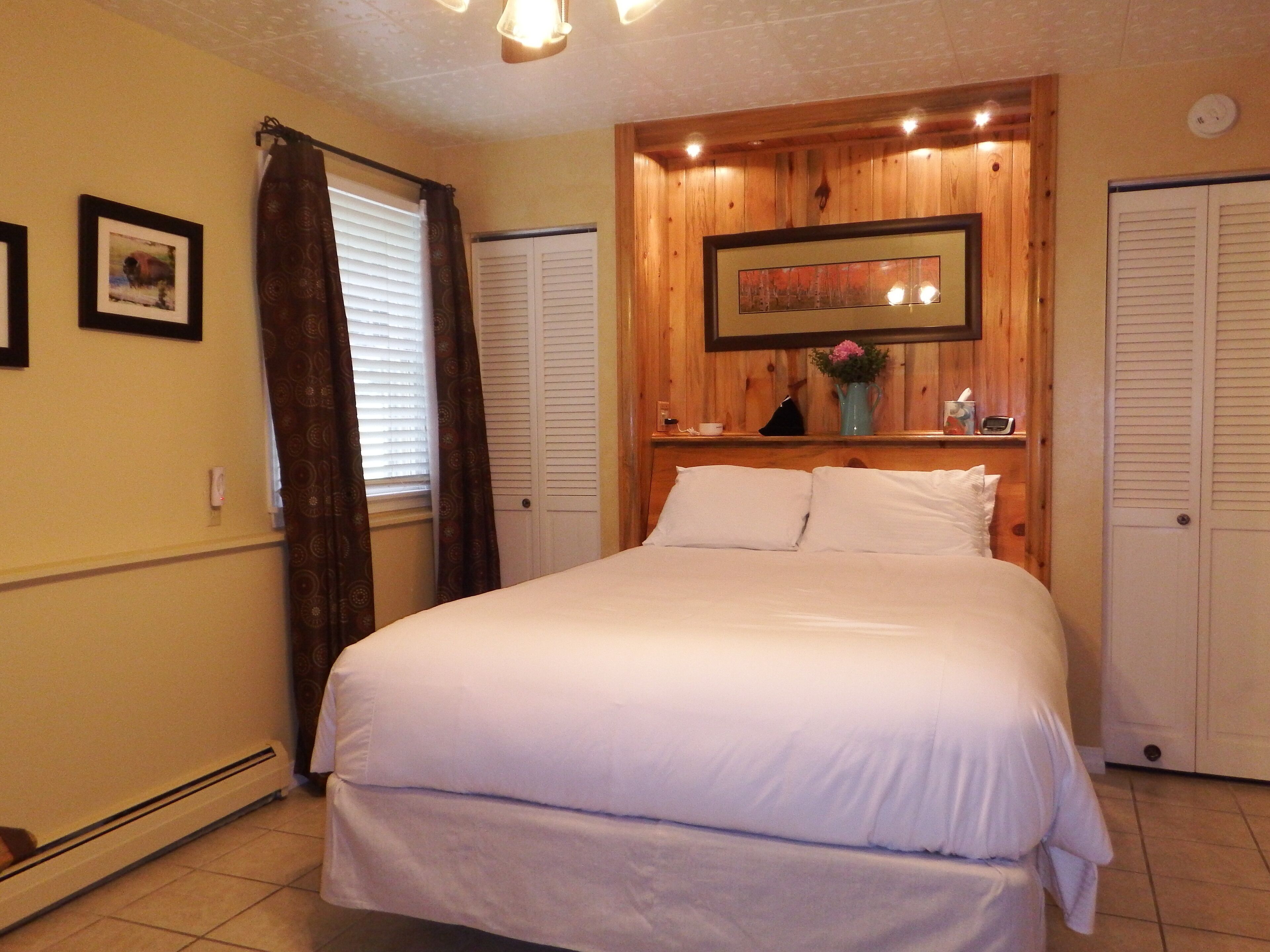 A bedroom with a large bed, wooden headboard, a small table with a vase, and two doors.