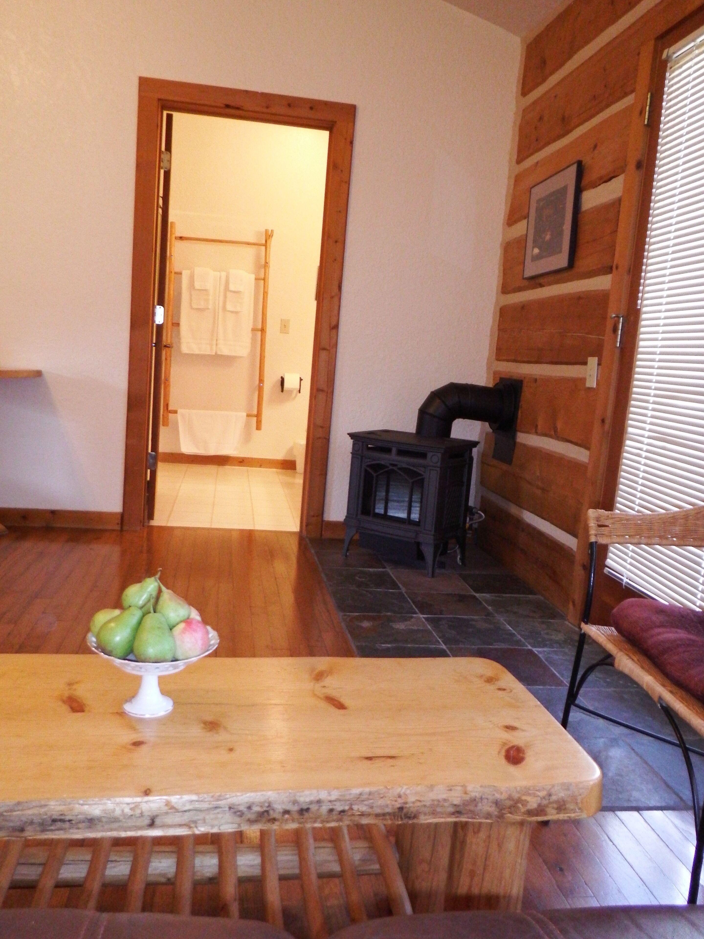 A wooden dining table with a fruit bowl, a wooden bench, a chair, and a fireplace.