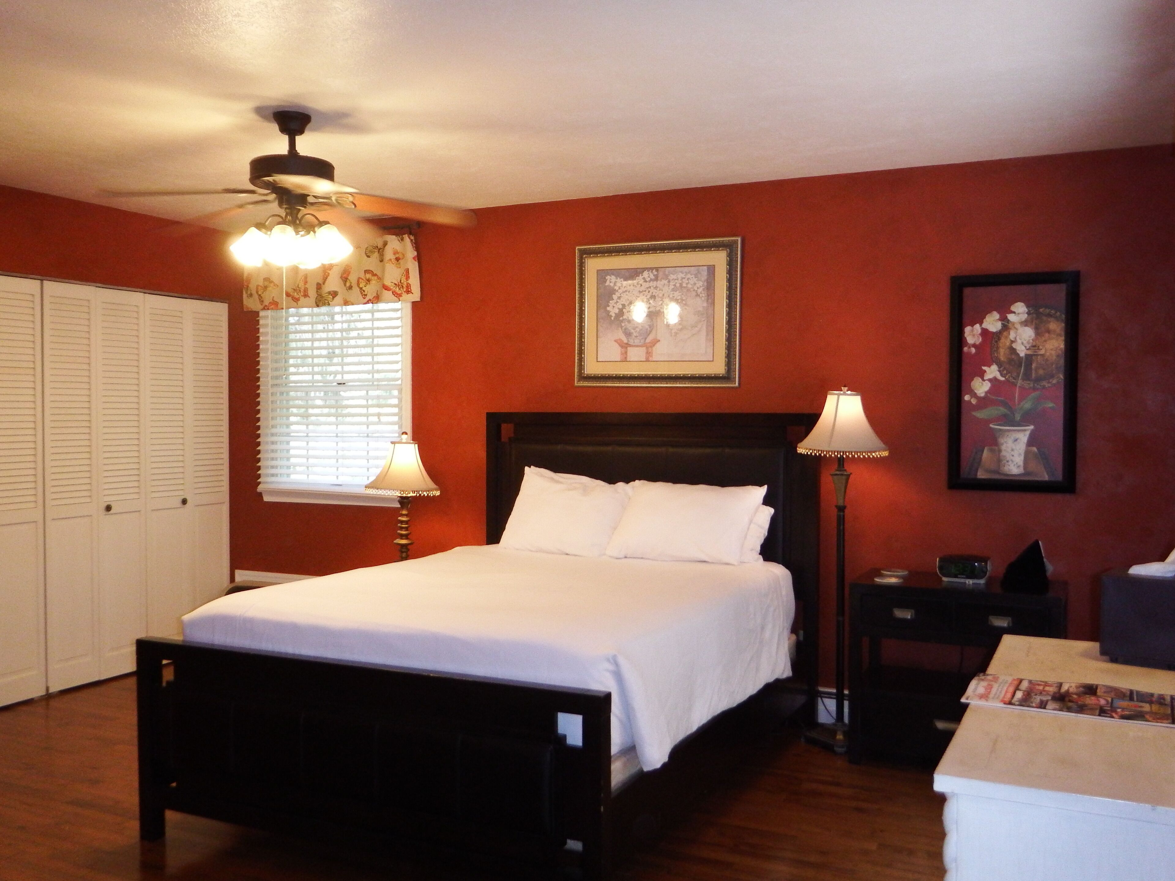 A bedroom with a bed, bedside lamps, a nightstand, a framed picture on the wall, and a window with blinds.