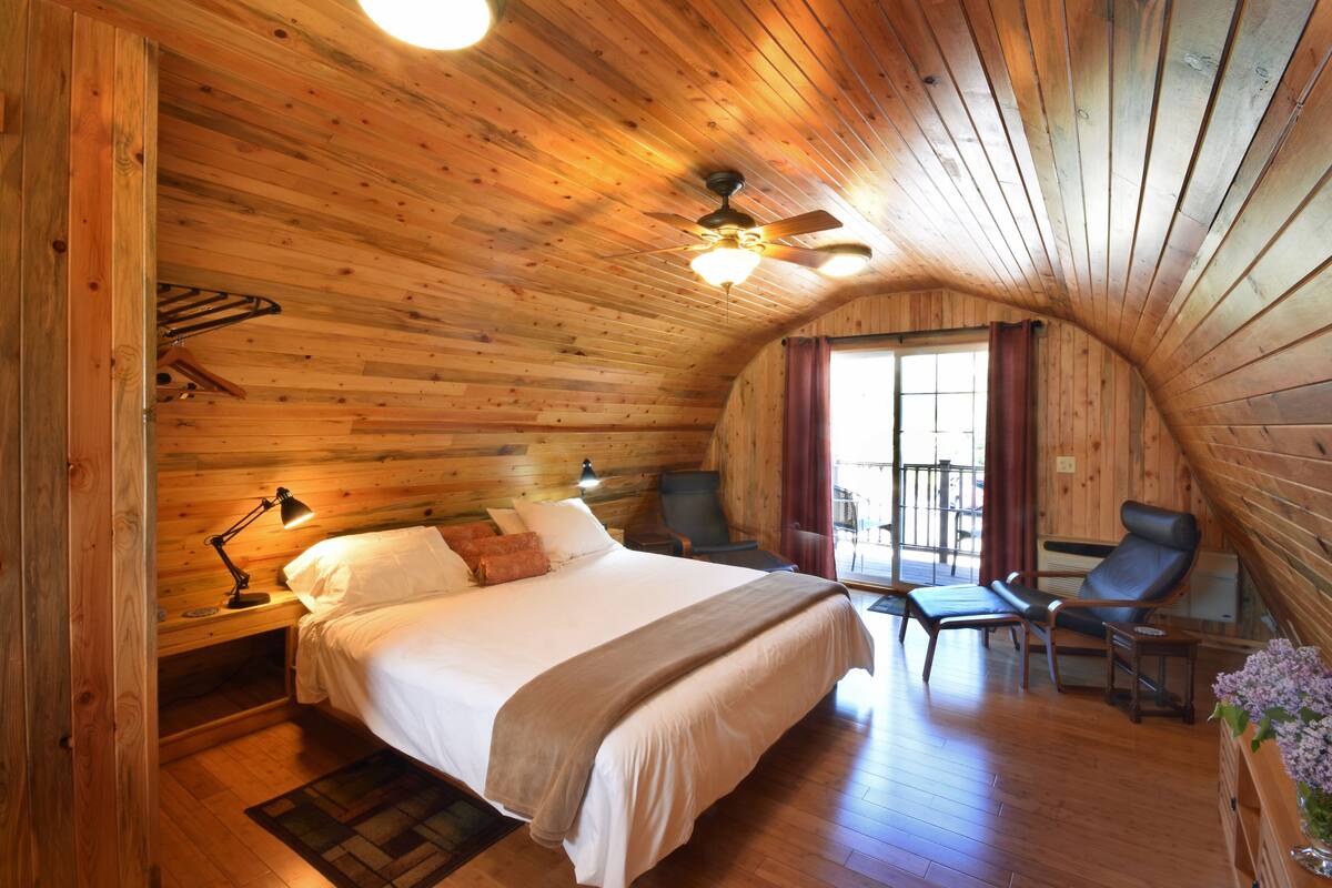 A cozy log cabin bedroom with a bed, bedside tables, a desk, and a chair.