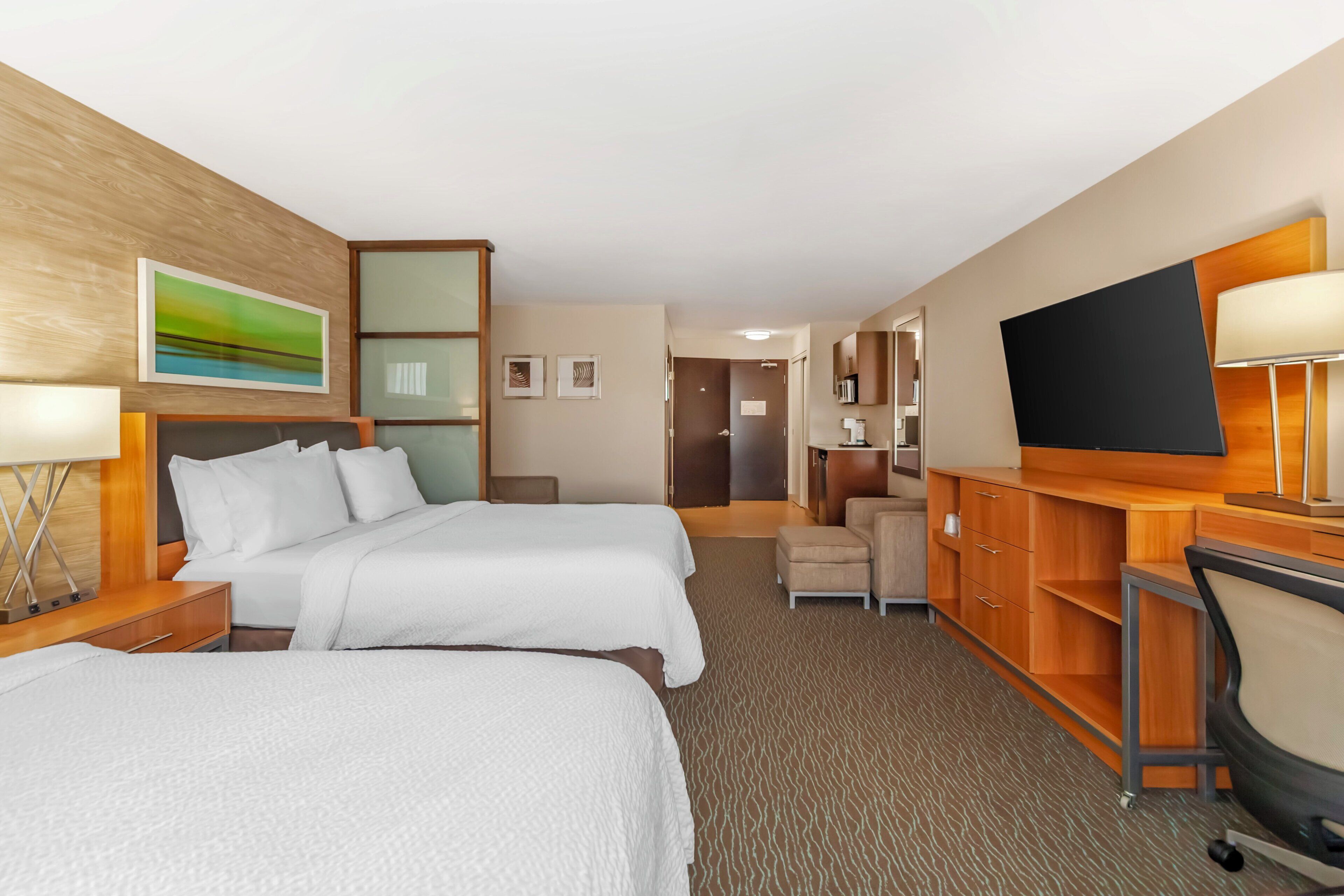 A hotel room with two beds, a desk, a TV, and a small seating area.