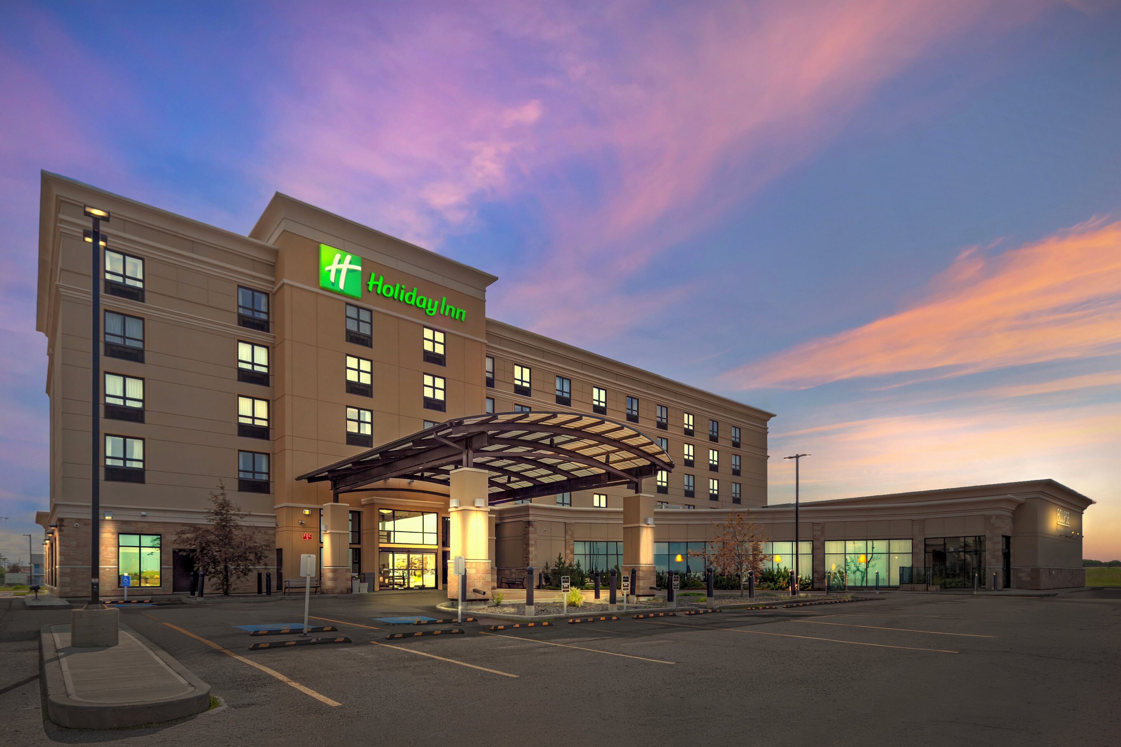 A hotel with a covered entrance, multiple windows, and a parking lot.