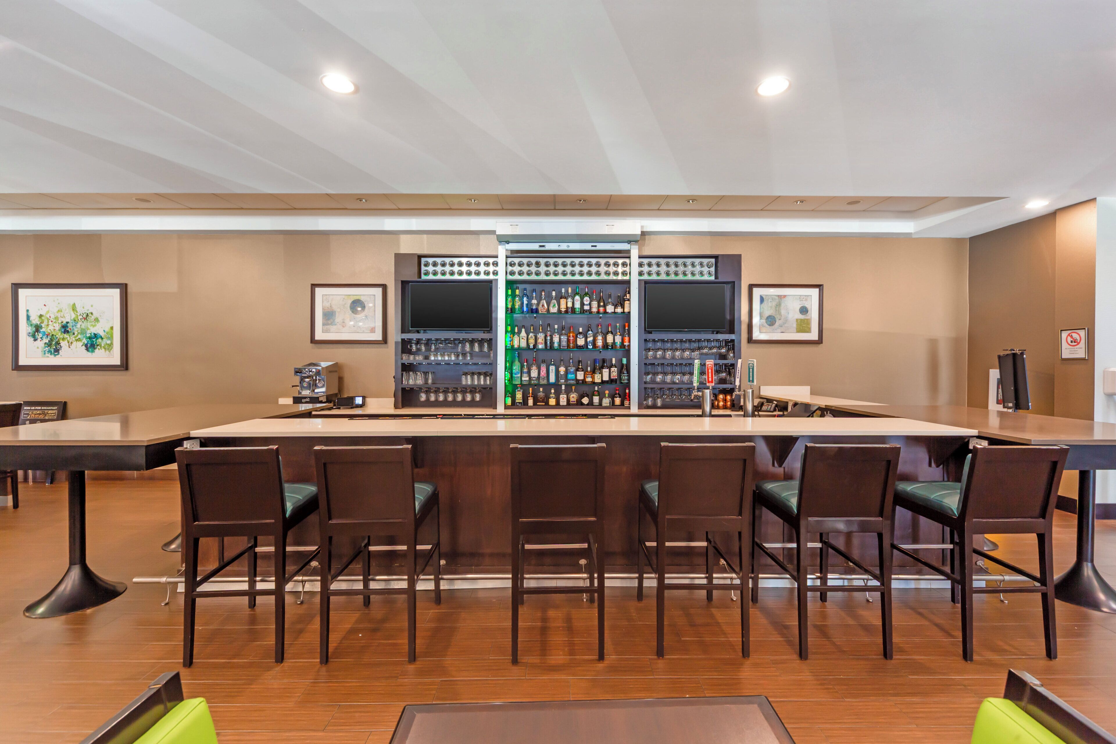 Een bar met een lange toonbank, meerdere stoelen en een divers assortiment aan flessen en glazen.