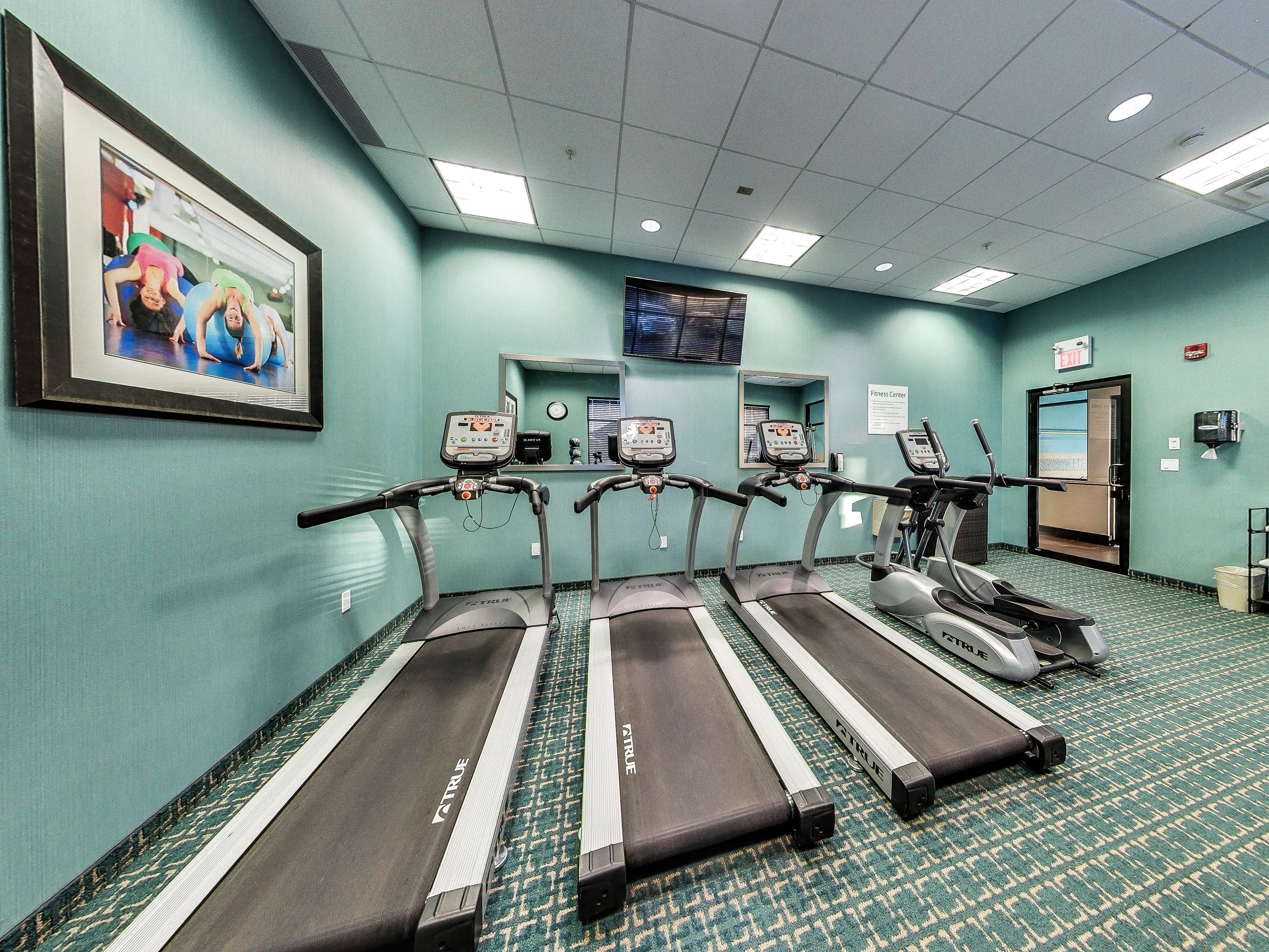 A fitness center with treadmills and exercise equipment, a clock, and a framed picture on the wall.