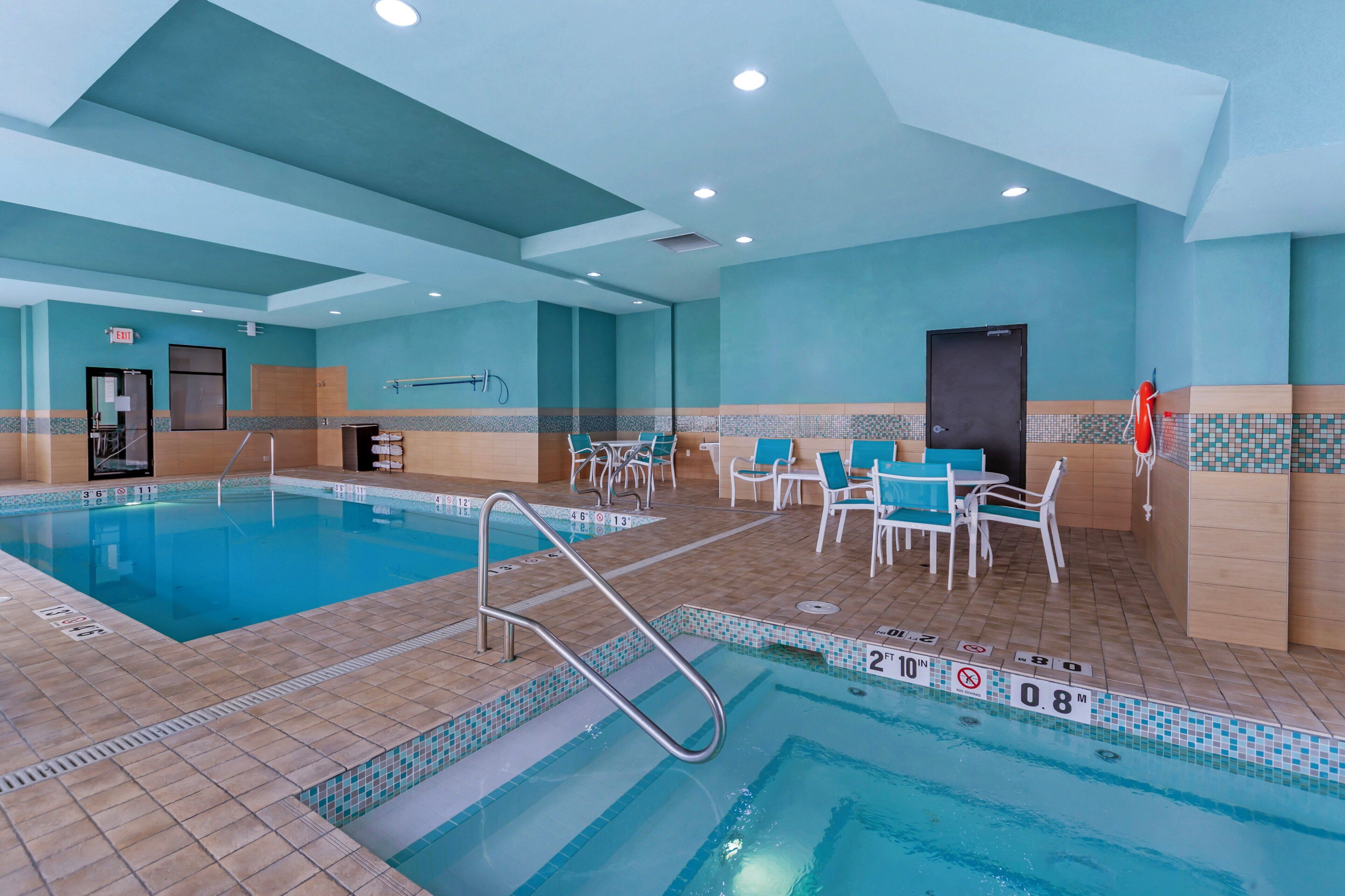 Una piscina interior con trampolín, sillas de descanso y suelo de baldosas.
