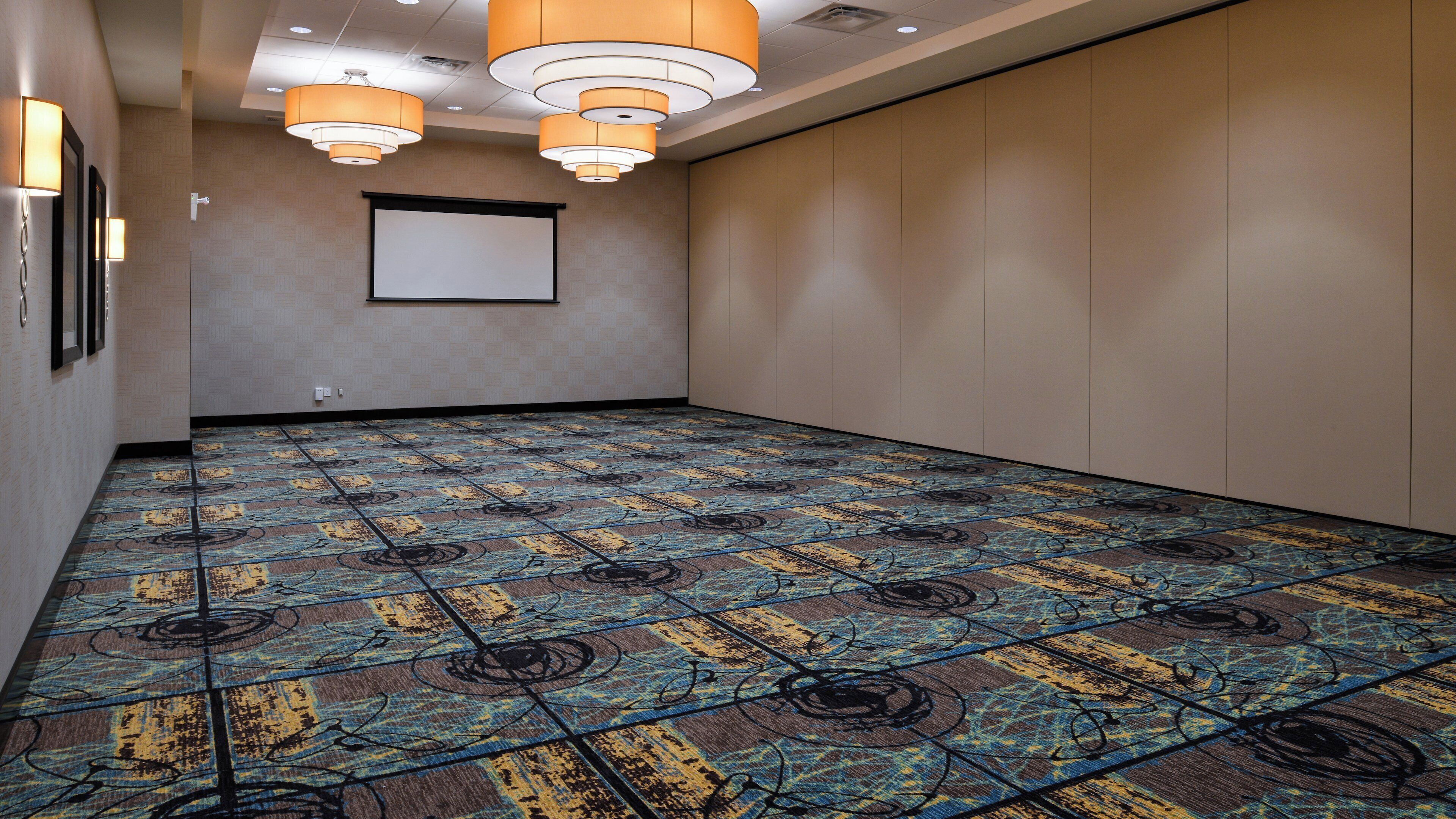 Una sala de conferencias con alfombra estampada, una pantalla de proyector e iluminación empotrada.