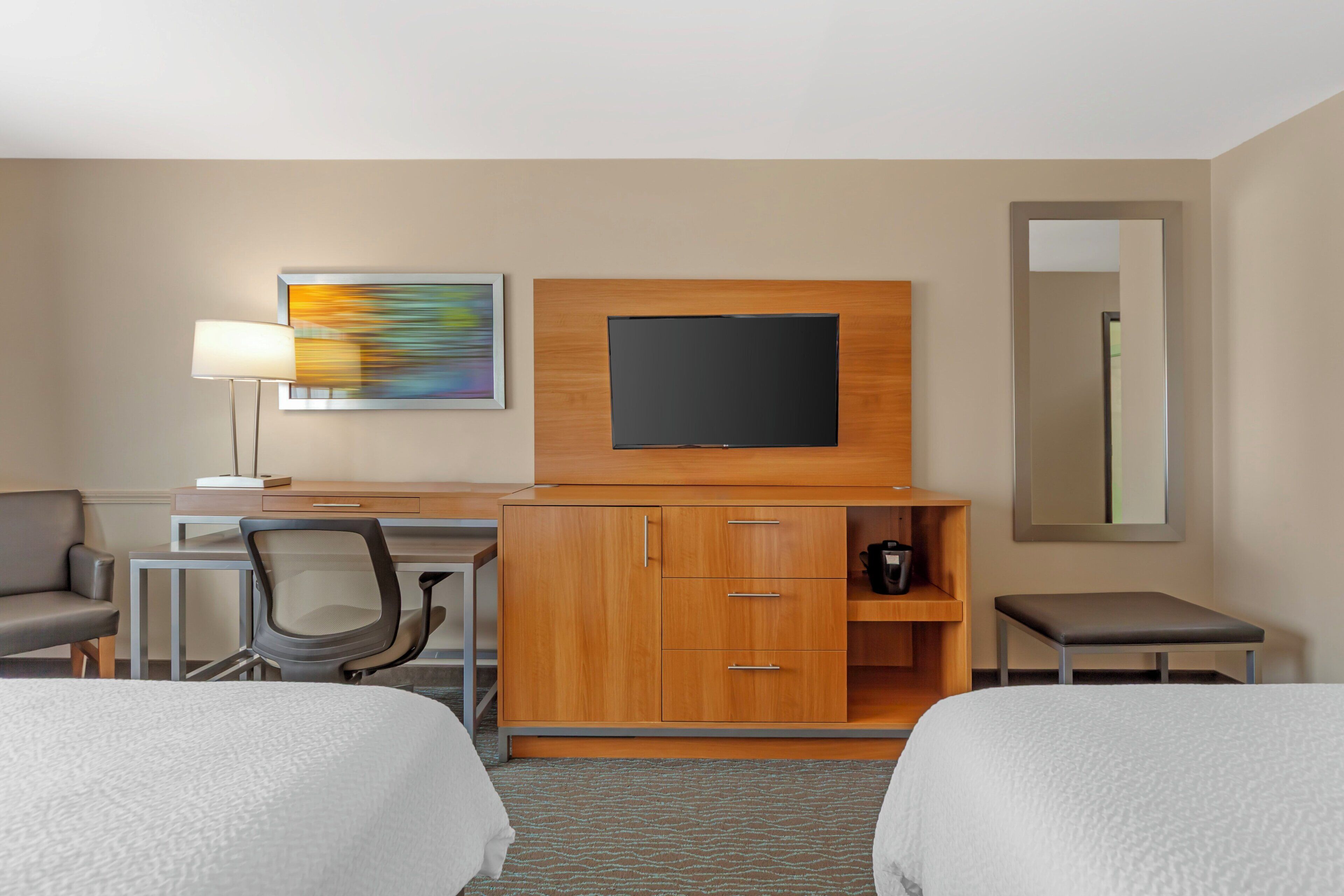 A hotel room with a bed, desk, chair, television, and a small table.