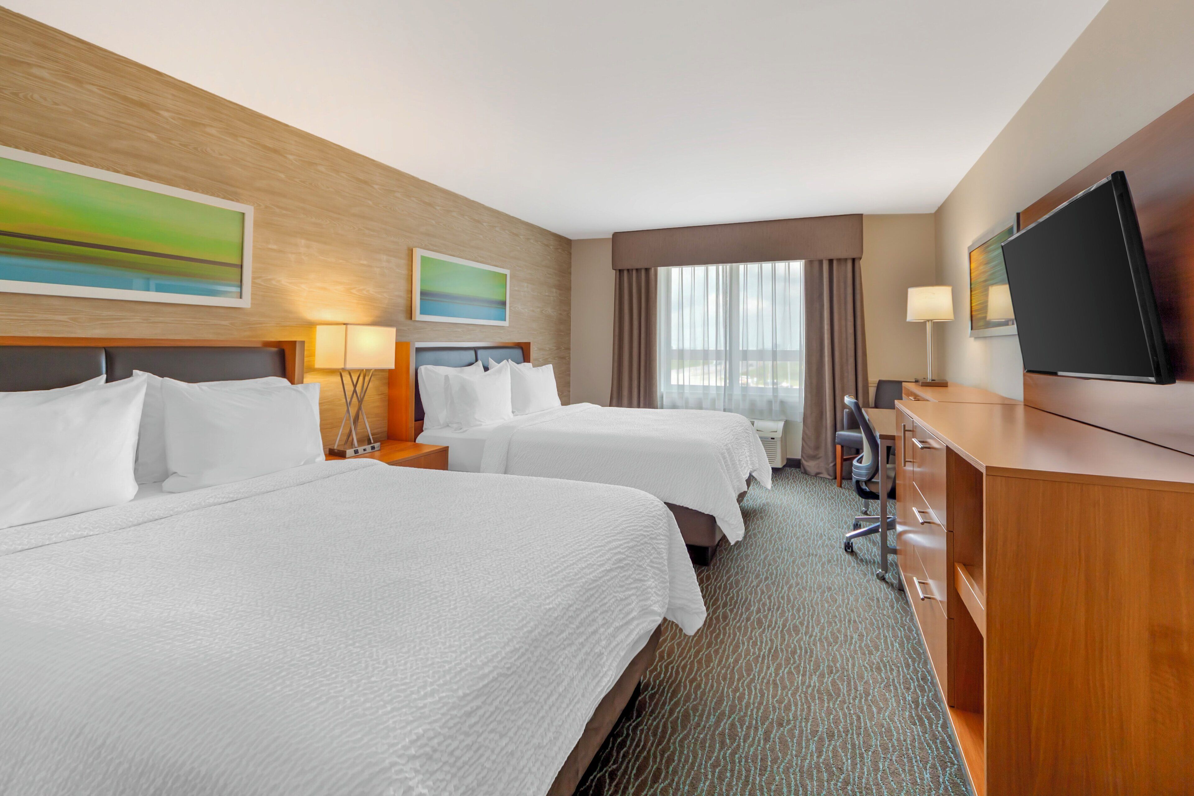 A hotel room with two beds, a desk, a television, and artwork on the walls.