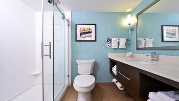 Un baño moderno con cabina de ducha de vidrio, inodoro blanco, tocador con espejo y dos cuadros enmarcados en la pared.