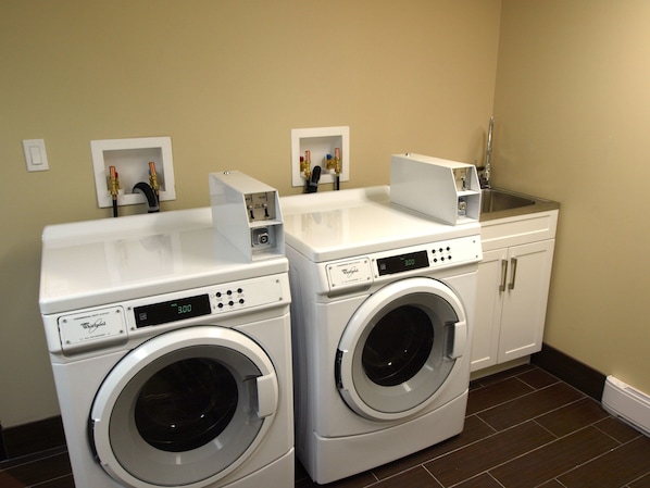 A laundry room with two front-loading Whirlpool washers, a sink, and a cabinet.