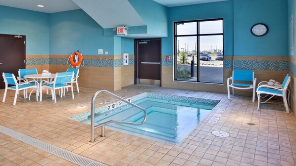A pool area with a tiled floor, a pool with a safety ladder, and blue chairs around a table. - Holiday Inn Hotel & Suites Edmonton Airport & Conference Ctr by IHG (Nisku)