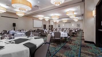 A conference room with multiple tables set for dining, equipped with chairs, and overhead lighting fixtures.
