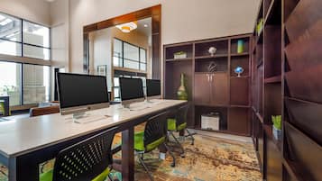 Un espacio de oficina moderno con varias Apple iMacs sobre una mesa larga, sillas ergonómicas, un espejo grande y una estantería con objetos decorativos.