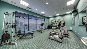 A gym with exercise equipment, a patterned carpet, and a large window with blinds. - Holiday Inn Hotel & Suites Edmonton Airport & Conference Ctr by IHG (Nisku)