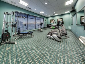 A gym with exercise equipment, a patterned carpet, and a large window with blinds. - Holiday Inn Hotel & Suites Edmonton Airport & Conference Ctr by IHG (Nisku)