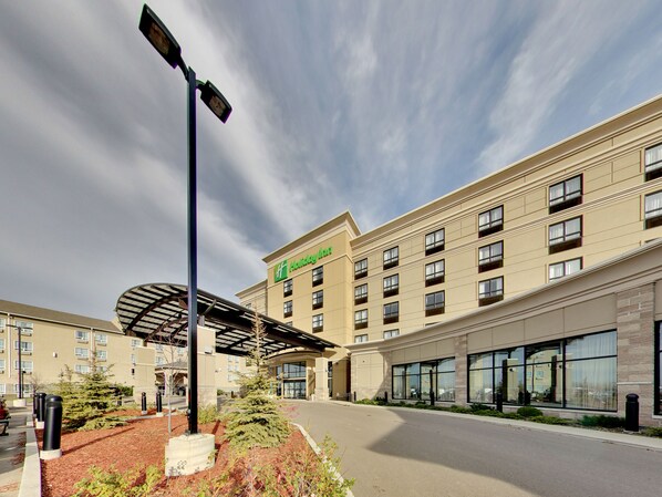 Un hotel Holiday Inn con entrada cubierta, varios pisos y una zona ajardinada con plantas.