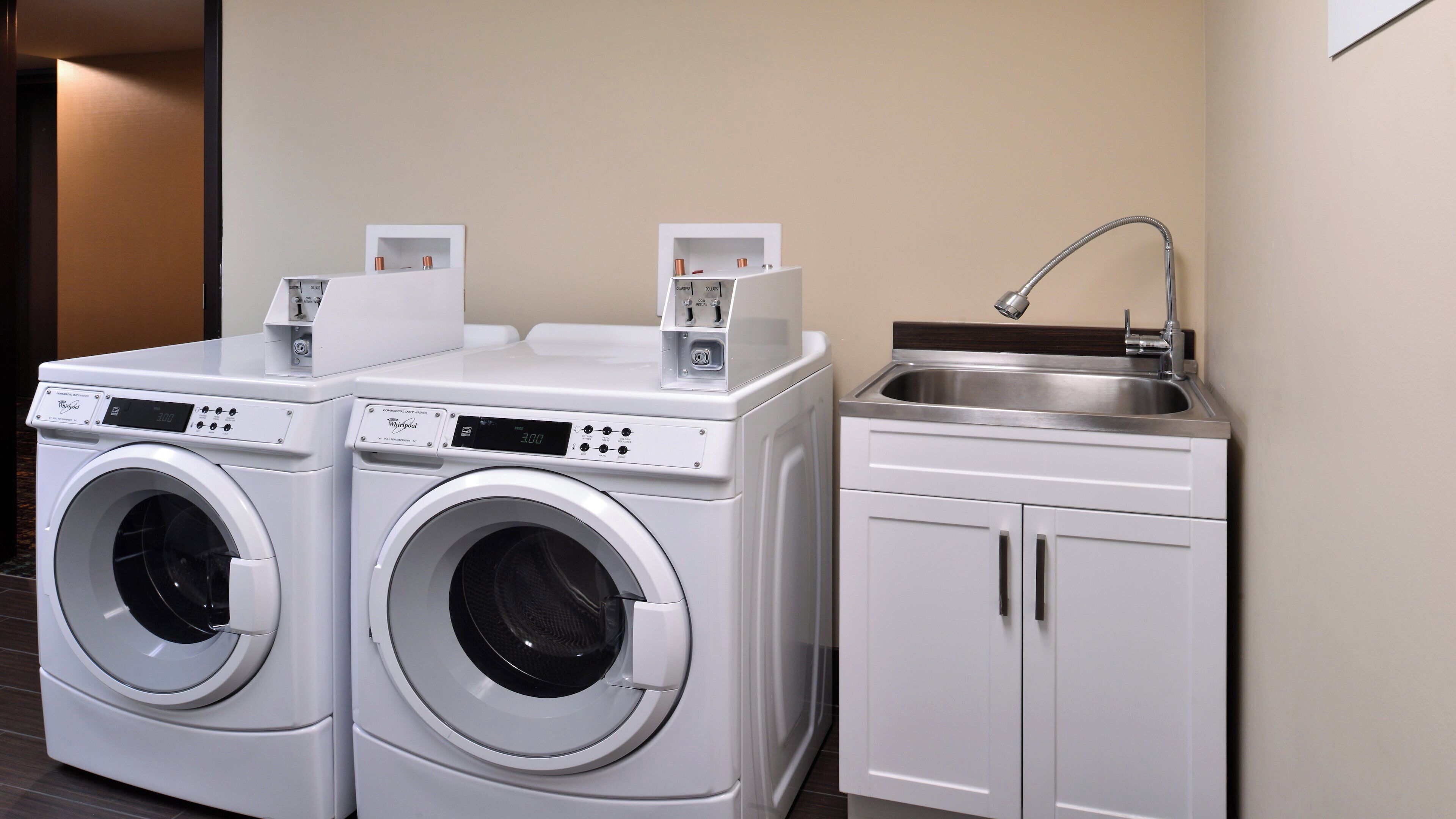 A laundry area with two front-loading washing machines and a built-in stainless steel sink.