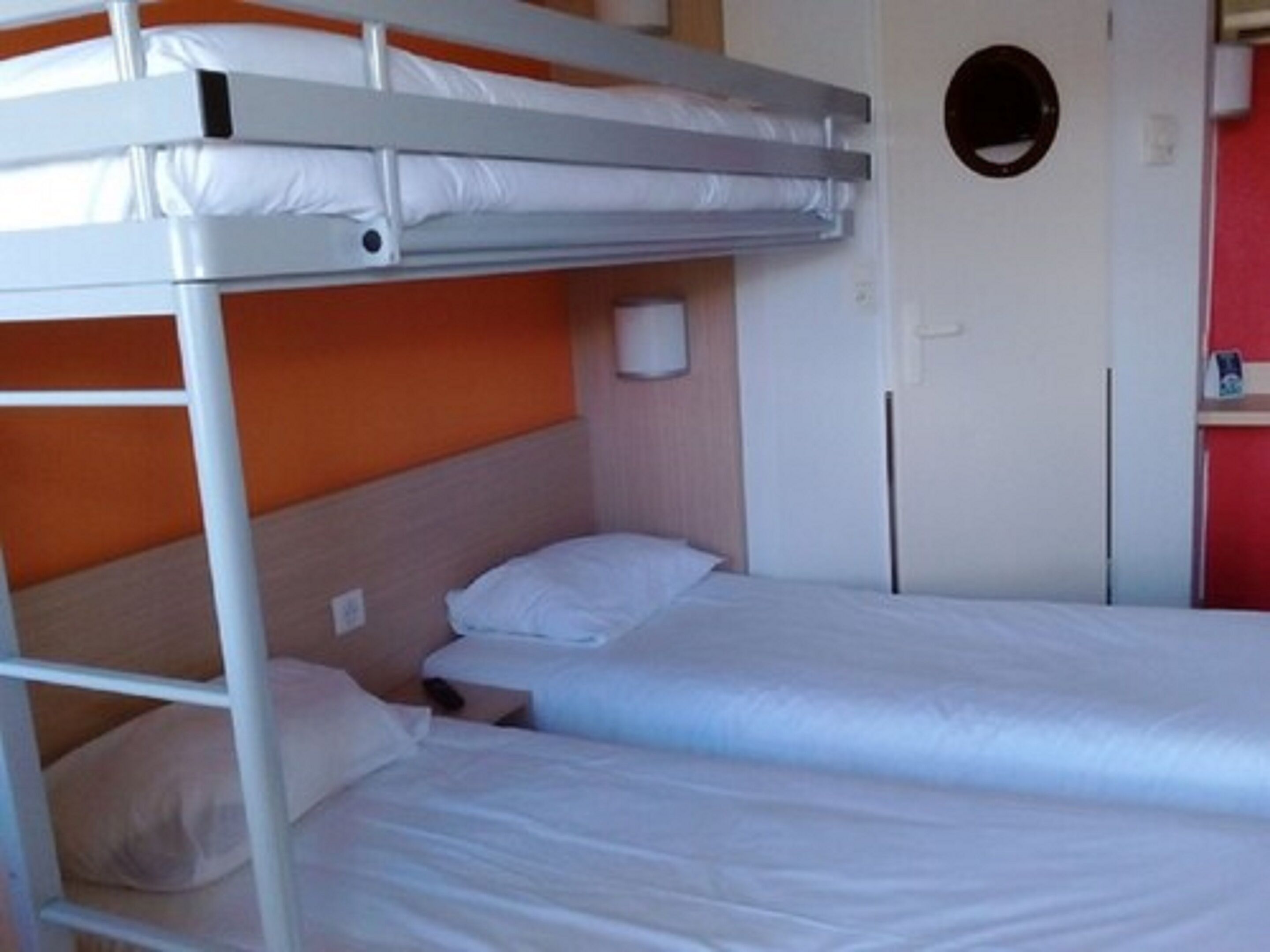 Una cama litera con ropa de cama blanca, cabecera de madera y pared roja.
