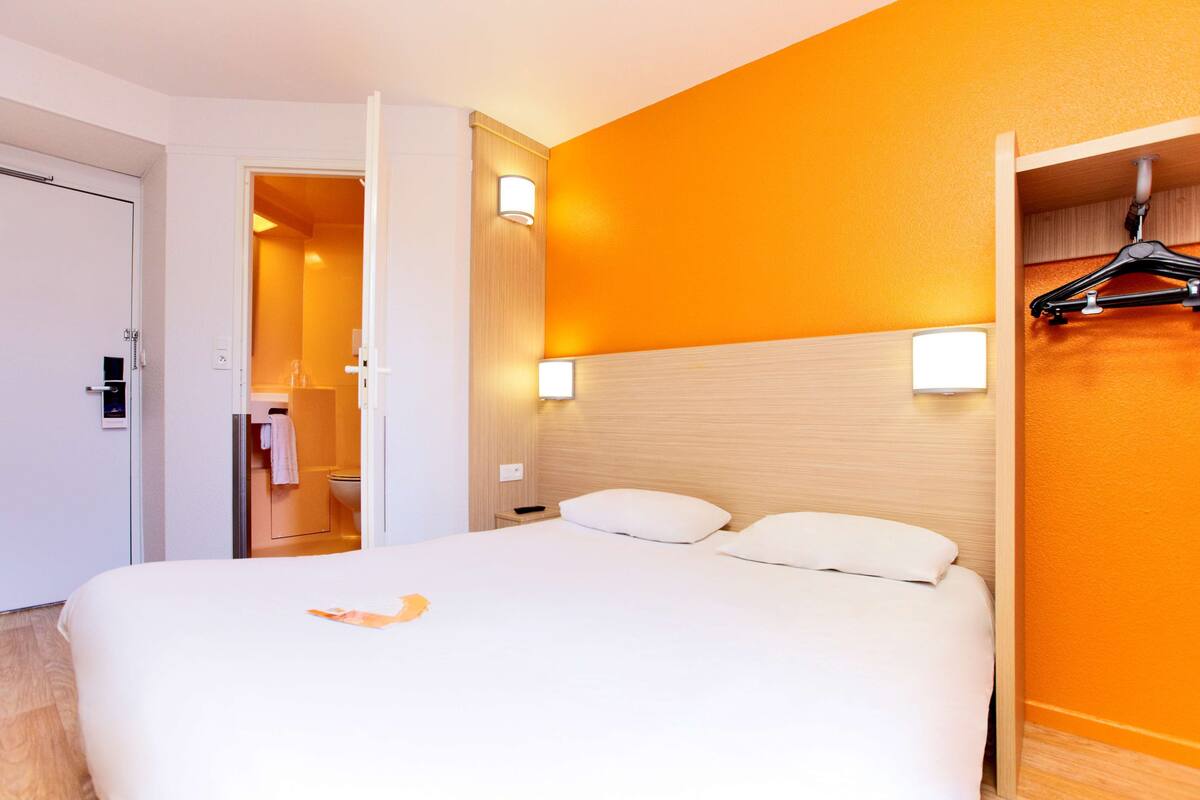 Habitación de hotel con una cama grande, cabecera de madera, dos lámparas de noche y un perchero.