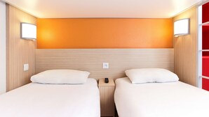 Habitación de hotel con dos camas, cabecero de madera y una pared de acento roja.