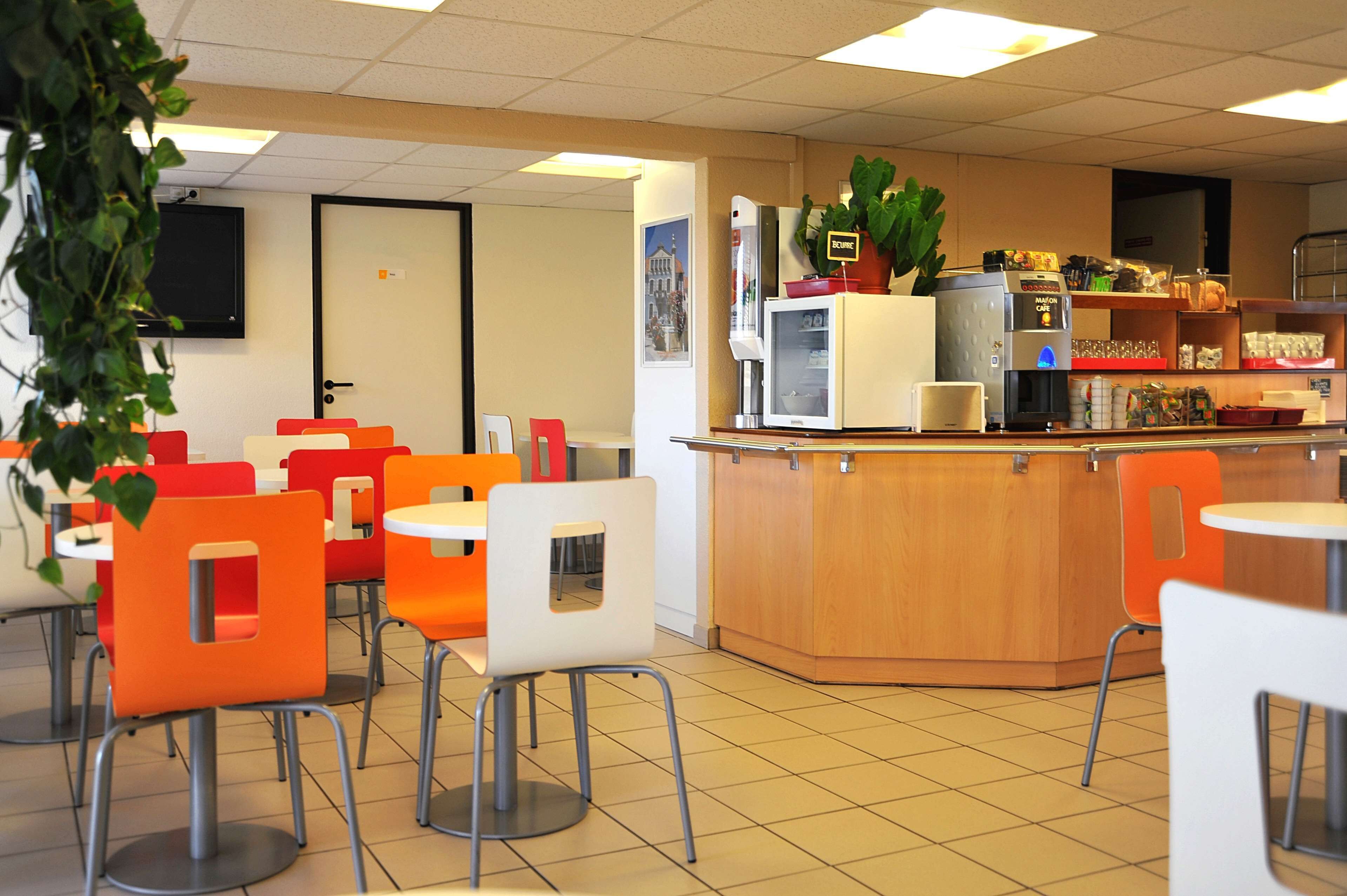 Een café met oranje en witte stoelen, een houten toonbank en een koelkast met een koffieapparaat.