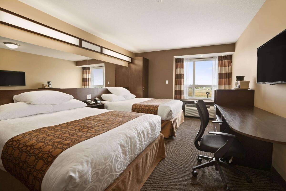 Habitación de hotel con dos camas, un escritorio, una silla, un televisor y una ventana con vistas.