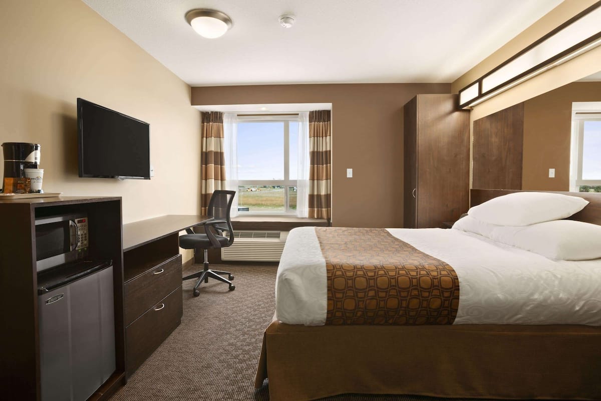 Habitación de hotel con cama, escritorio con computadora, televisor y ventana con cortinas.