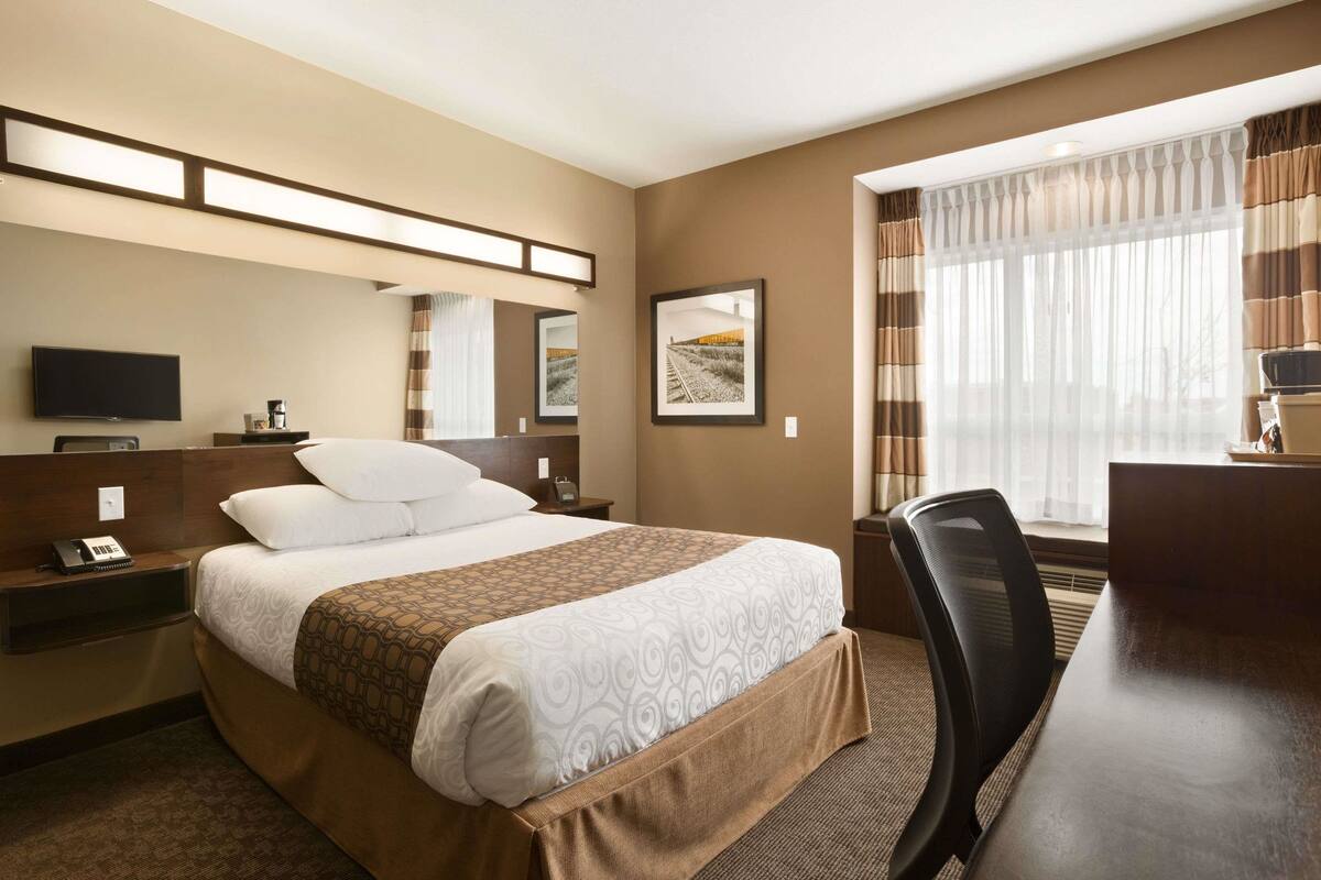Una habitación de hotel con una cama grande, un escritorio, una silla, un televisor y una ventana con cortinas.