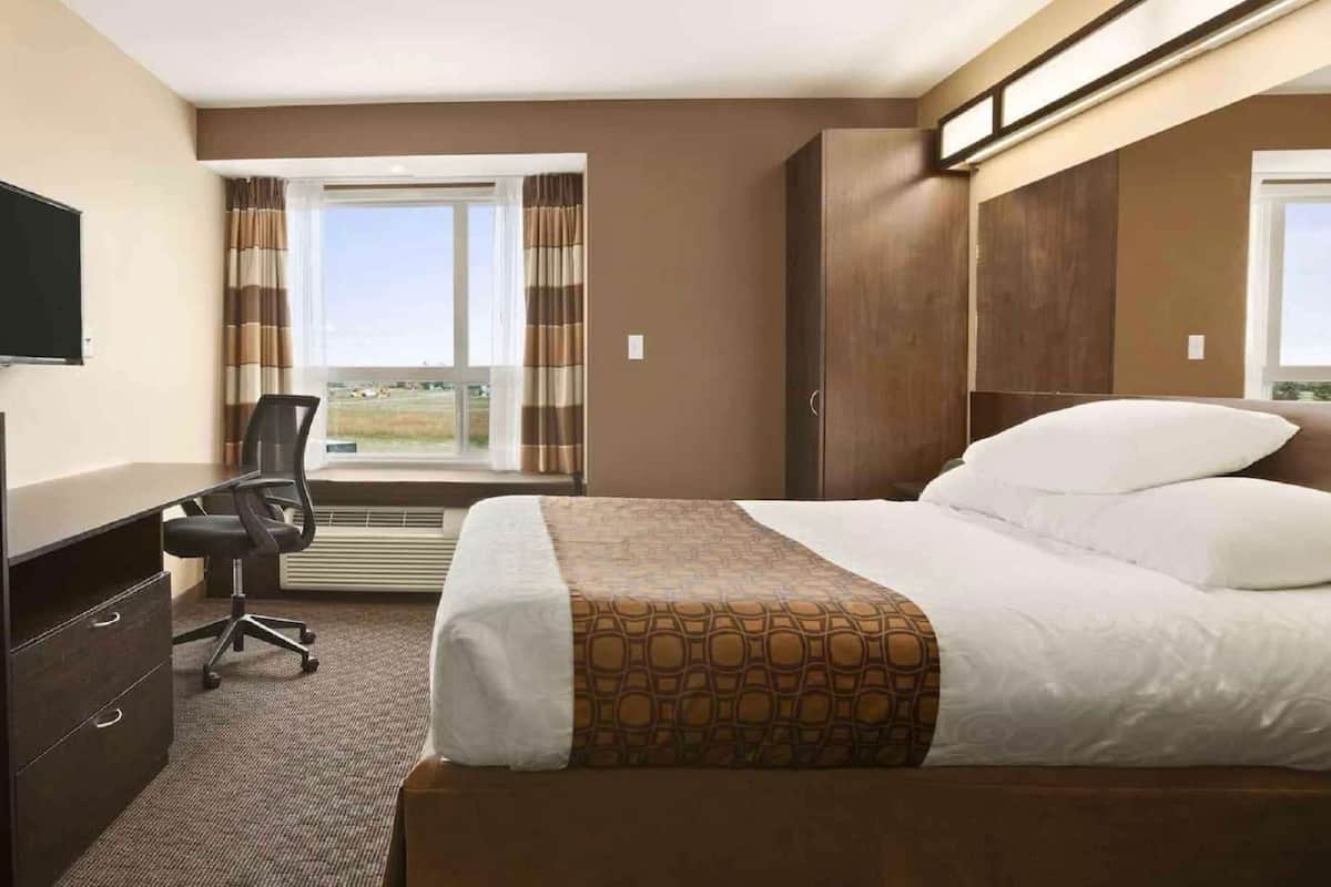 Habitación de hotel con cama, escritorio con silla, televisor y ventana con cortinas.