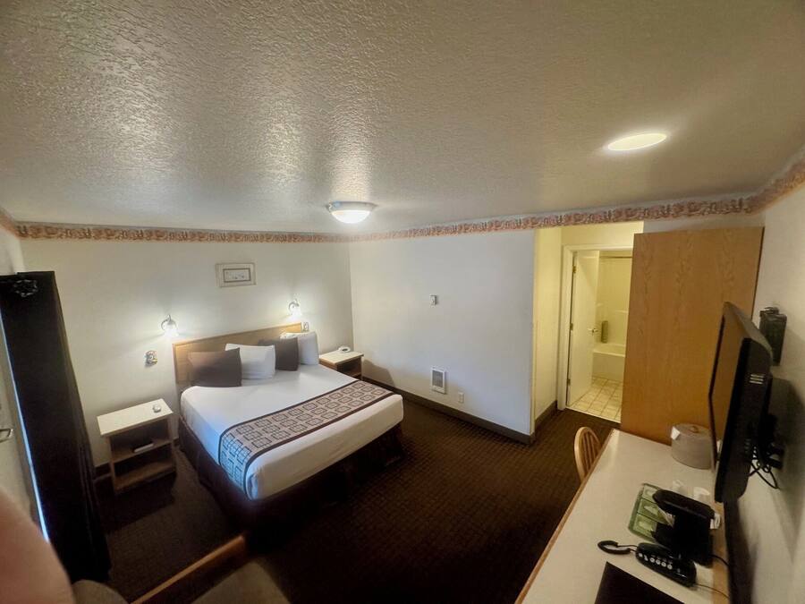 A hotel room with a bed, a desk with a computer, a chair, a TV, and a bathroom door.