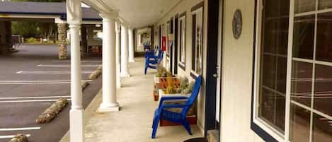 Un espacio al aire libre cubierto con una fila de sillas azules y una mesa, un estacionamiento y un edificio con grandes ventanales.