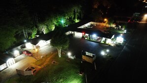 Vista nocturna de un hotel con estacionamiento, zona de estar al aire libre y un pequeño jardín.