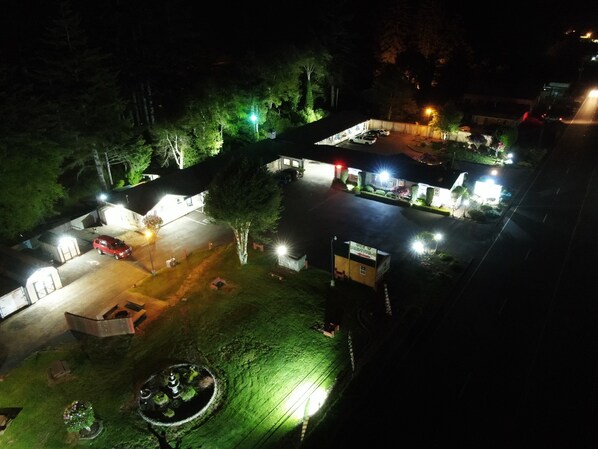 A nighttime view of a hotel with a parking lot, outdoor seating area, and a small garden. - Ocean Breeze Motel (Florence)