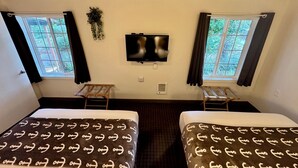 Una habitación de hotel con dos camas, televisión y ventanas con cortinas.