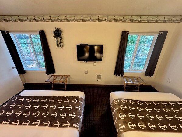 Una habitación de hotel con dos camas, televisión y ventanas con cortinas.