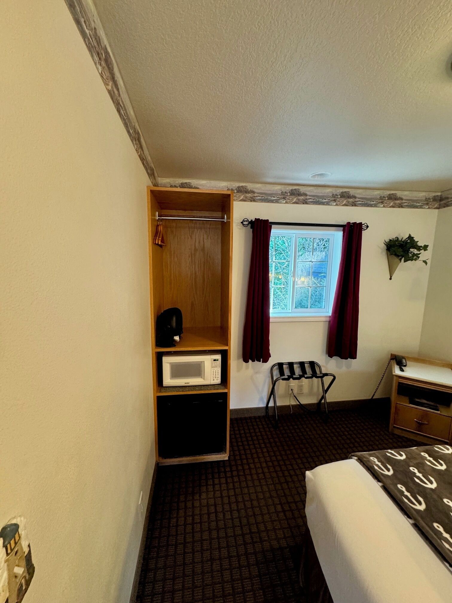 A compact hotel room with a bed, a small desk, a microwave, a chair, and a wardrobe.