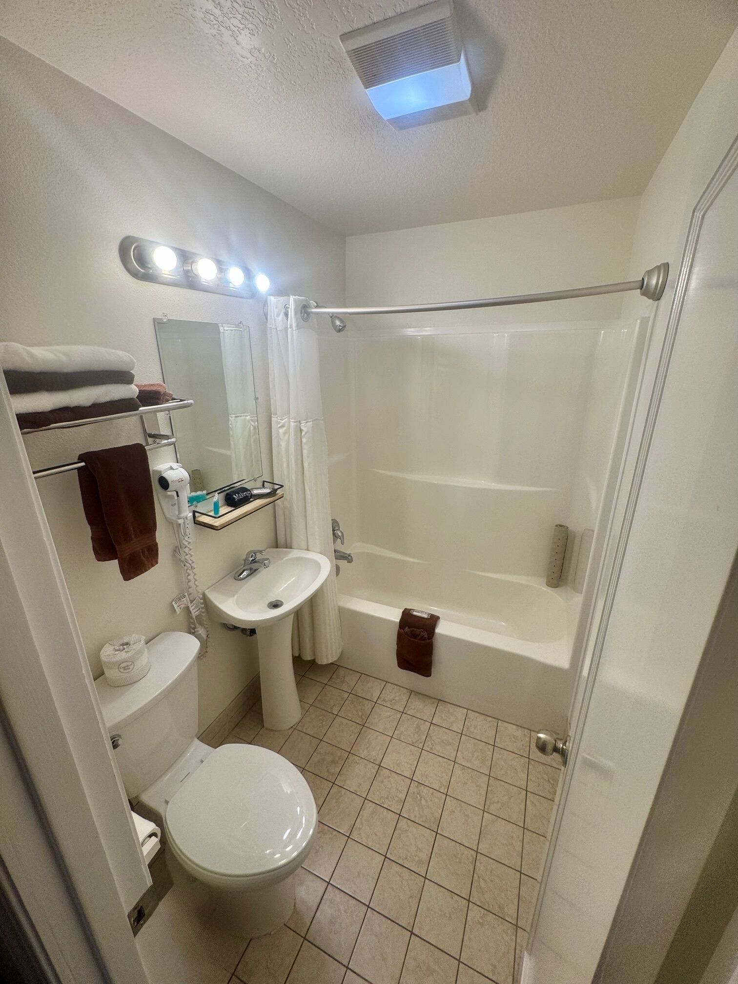 Un baño con inodoro, lavamanos y bañera. Hay un perchero con toallas, un espejo y una cortina de ducha.